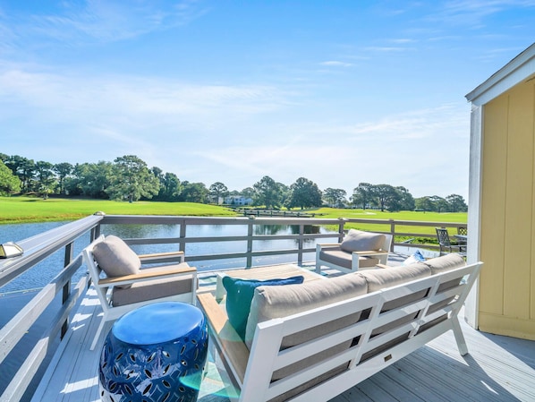 A deck with outdoor seating, a view of a golf course, and a body of water.
