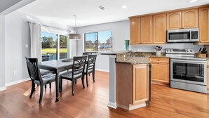 A modern kitchen with wooden cabinets, stainless steel appliances, and a dining area with a table and chairs. - Bay View, Six-Seat Golf Cart, Pet Friendly, Linkside Village 434 (Miramar Beach)