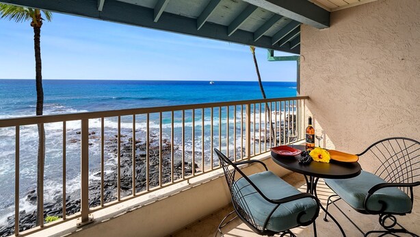A balcony with a view of the ocean, a table with a bottle and glasses, and two chairs.