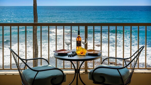A balcony with a table set for two, overlooking the ocean.