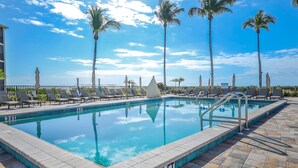 A swimming pool with lounge chairs and palm trees, surrounded by a tiled deck. - SUNDIAL D306 - Lovely Sundial Sanibel Condo. Short Walk to Beach (Sanibel)