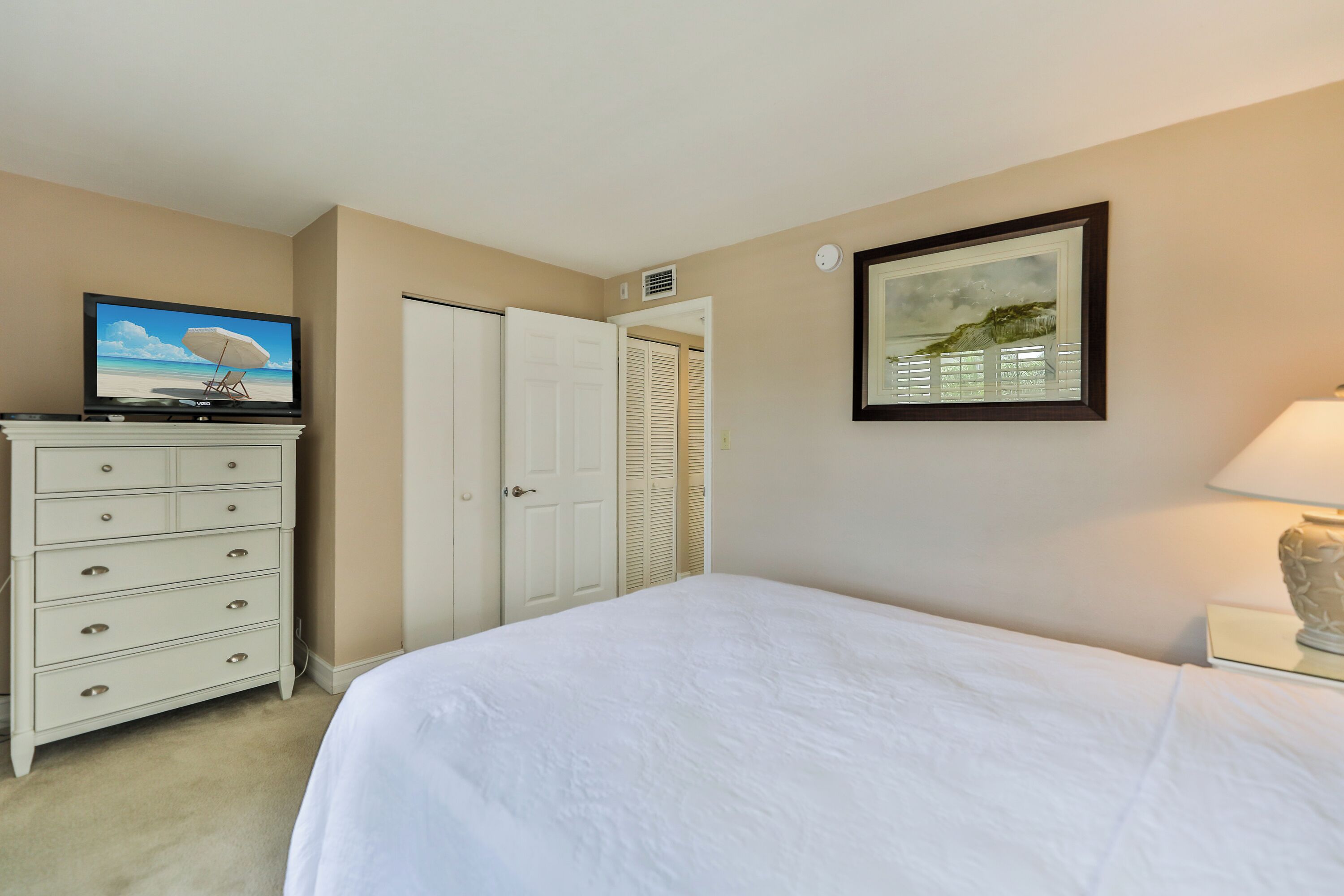 A bedroom with a bed, a dresser, a television on the dresser, a door, and a framed picture on the wall.