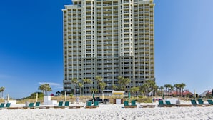 Un grand hôtel doté de nombreux balcons, une plage de sable devant et des palmiers.
