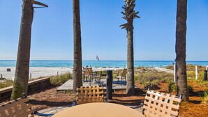 Une terrasse au bord de la plage, avec des chaises et une table en bois, d’où l’on a une vue sur l’océan.