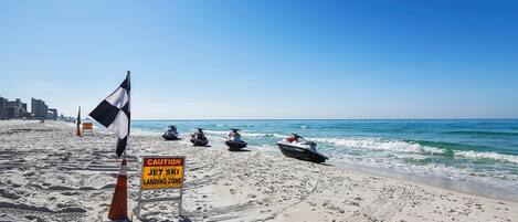 Una playa con motos acuáticas, un letrero de precaución y un cielo azul despejado.