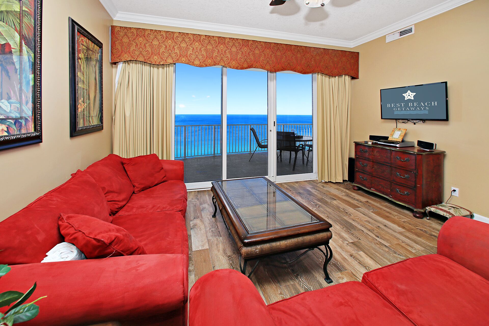 A living room with a red sofa, a glass coffee table, and a view of the ocean through a sliding glass door.