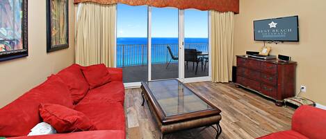 A living room with a red sofa, a glass coffee table, and a view of the ocean through a sliding glass door.