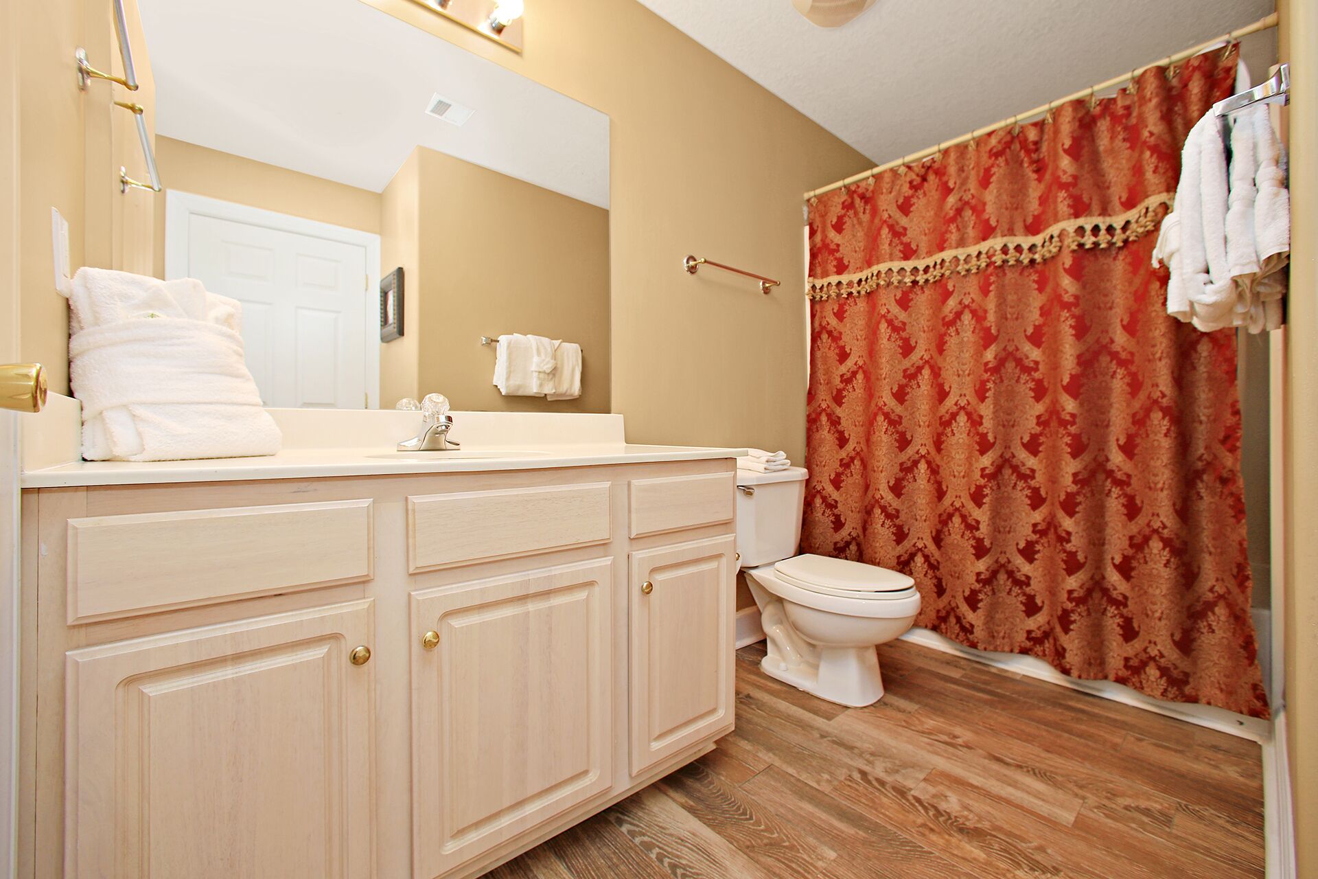 A bathroom with a wooden vanity, a toilet, and a shower curtain.