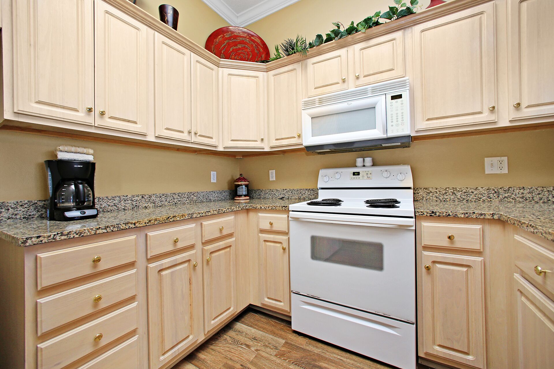 A kitchen with light wooden cabinets, a white stove, a microwave, and a coffee maker.
