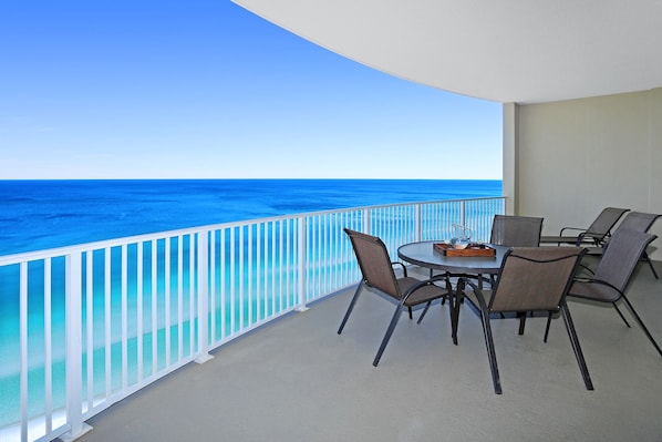Un balcon avec vue sur l’océan, une table ronde avec des chaises et une petite table avec une carafe et un plateau.