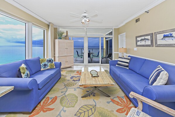 A room with two blue sofas, a wooden coffee table, and a view of the ocean through large windows.