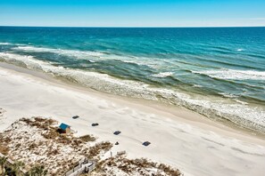 A beach with clear blue water, sandy shore, and a few beach huts.