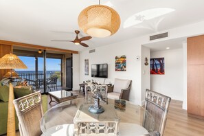 Ein modernes Wohnzimmer mit einem Glastisch, Korbstühlen, einem Deckenventilator und Kunstwerken an den Wänden.
