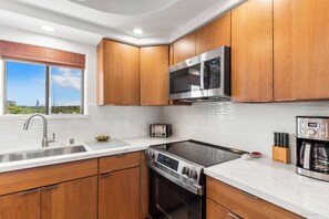 A modern kitchen with wooden cabinets, stainless steel appliances, a built-in oven, and a microwave. - Kihei Beach #510–Paradise with Modern Comfort-Completely Remodeled November 2024 (Kihei, Maui)