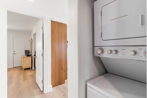 A laundry room with a front-loading washer and dryer, a wooden cabinet, and a door leading to another room.