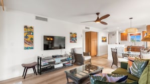 A spacious living room with a flat-screen TV, comfortable seating, and artwork on the walls.