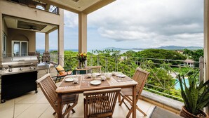 A balcony with a grill, dining table, chairs, and a view of a pool and mountains. - Matapalo 502♆Oceanview in the 🎔 of town♆ Huge Pool Beach acss (Tamarindo)