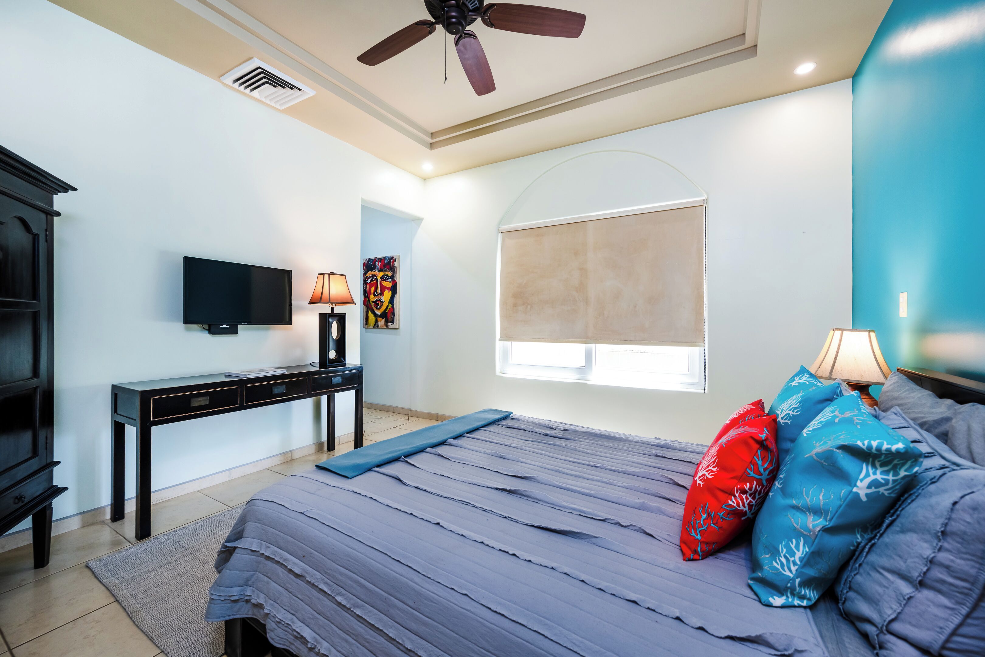 Une chambre à coucher comprenant un lit, un bureau, une télévision et un ventilateur de plafond.