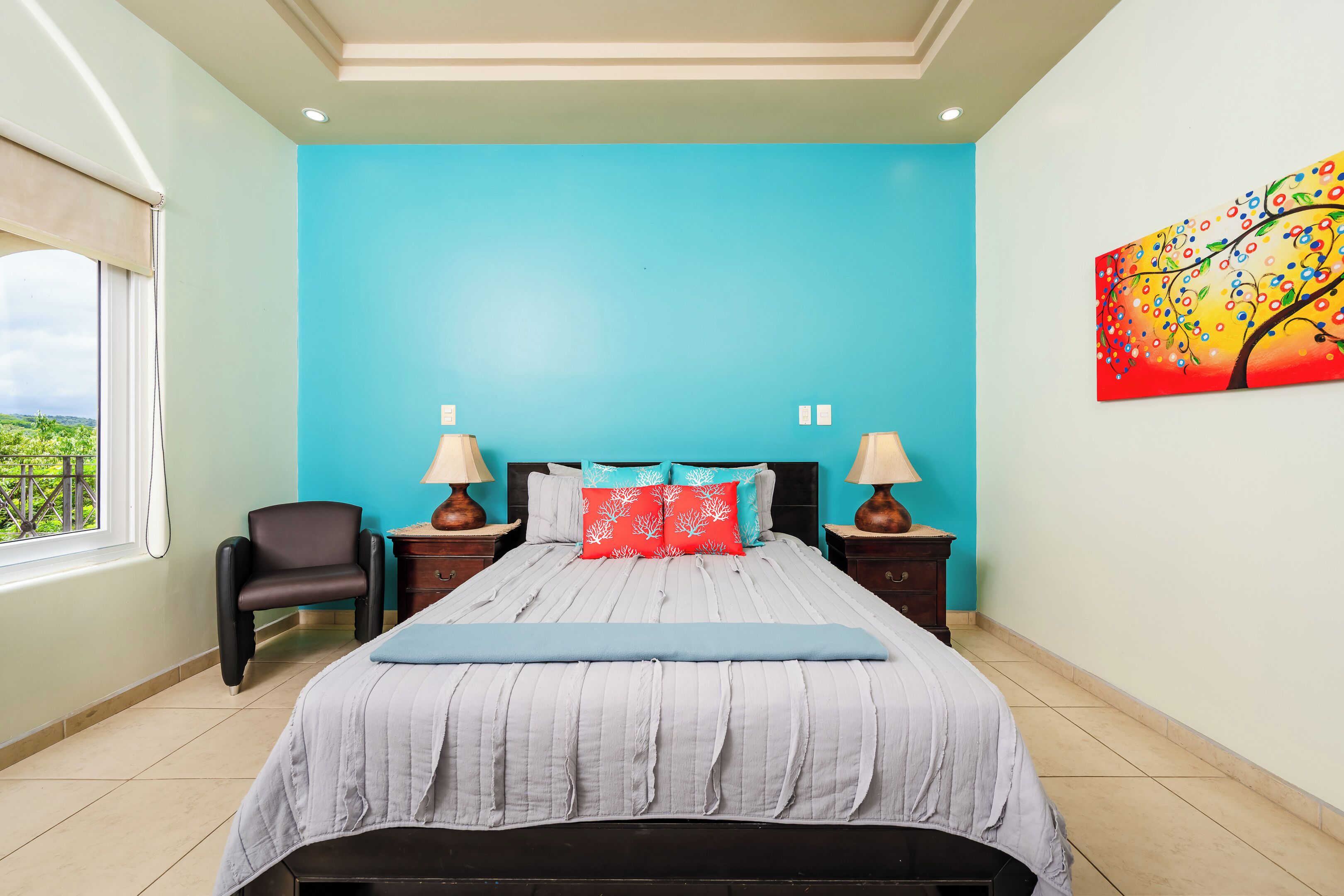 A bedroom with a large bed, two nightstands, a chair, and a window with a view.
