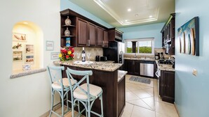 A modern kitchen with dark wood cabinets, a granite countertop, and a central island with two chairs. - Matapalo 502♆Oceanview in the 🎔 of town♆ Huge Pool Beach acss (Tamarindo)
