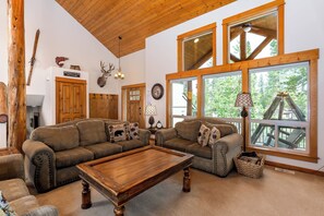 A cozy living room with a wooden ceiling, large windows, and a pool table.