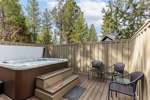 A wooden deck with a hot tub, steps, and wicker chairs.