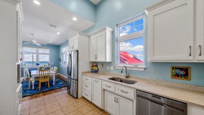 A kitchen with white cabinets, a stainless steel refrigerator, a dishwasher, and a window with a view of the sky. - Just Coastin: Great Gulf Views, Screened Porch, Pet Friendly (Cape San Blas)