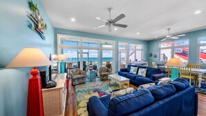 A spacious living room with a large blue sofa, a red floor lamp, and a view of the ocean through large windows. - Just Coastin: Great Gulf Views, Screened Porch, Pet Friendly (Cape San Blas)