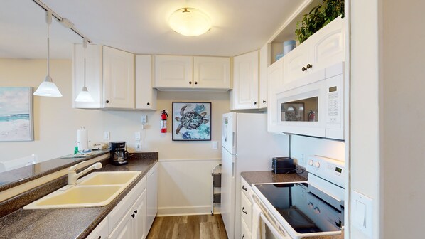 A compact kitchen with white cabinets, a microwave, a refrigerator, and a coffee maker.