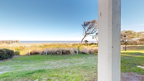 Un área verde con cerca de madera, un poste de luz y vista a la playa y al océano.