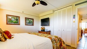 A hotel room with a bed, a ceiling fan, a TV, and a door leading to a balcony.