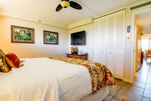 Una habitación de hotel con cama, ventilador de techo, televisión y puerta que da a un balcón.