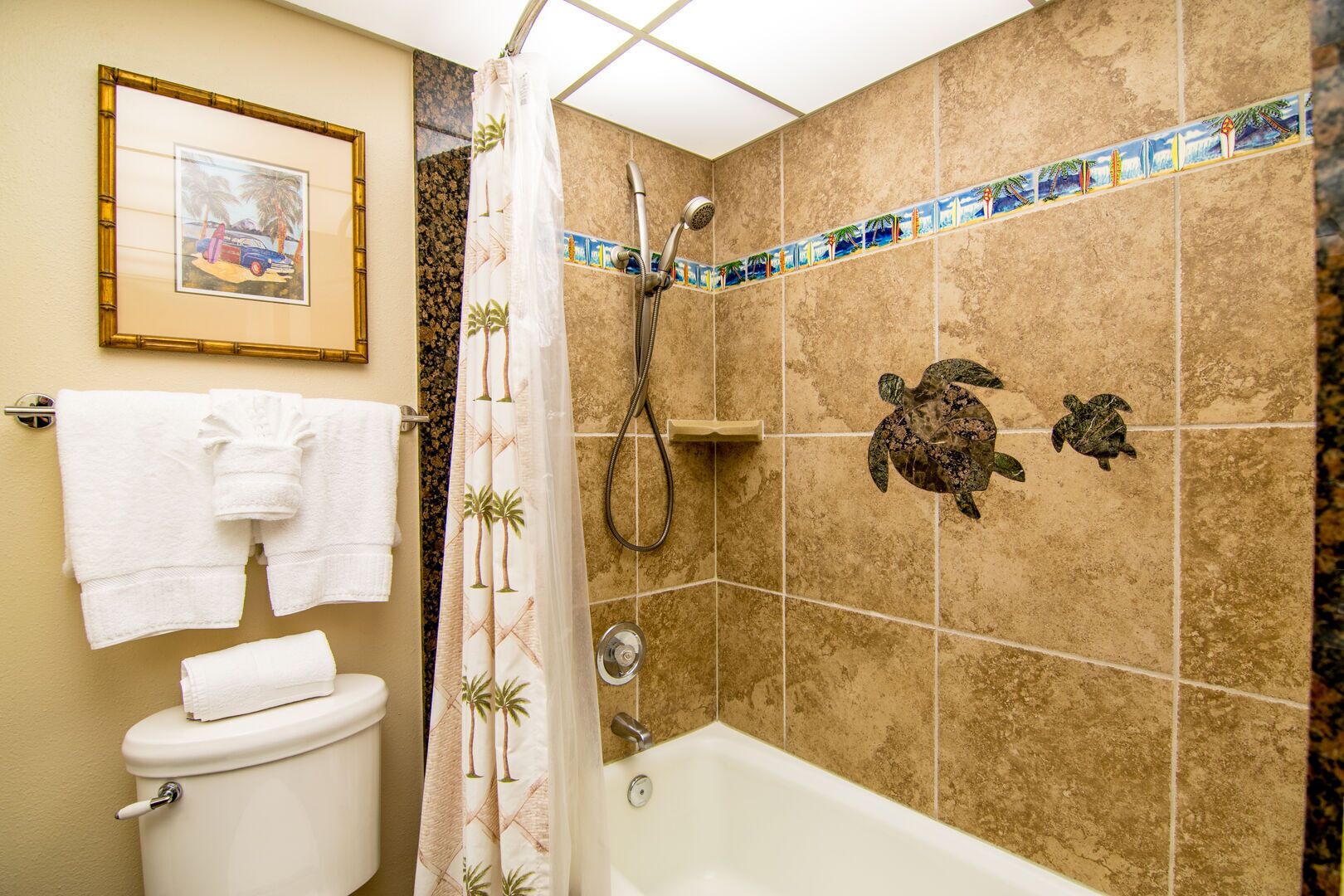 Une salle de bain équipée de toilettes, d’une baignoire et d’une douche. Des serviettes sont accrochées au mur et un cadre avec une image est placé au-dessus des toilettes.