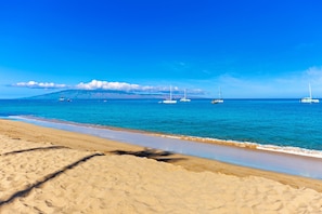 Een strand met helderblauw water, een zandstrand en diverse zeilboten.