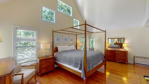 A four-poster bed with a canopy, a wooden nightstand with a lamp, a dresser with drawers, and a chair. - Hartnett Blvd 3502: 3  BR, 2  BA House in Isle of Palms, Sleeps 8 (Isle of Palms)