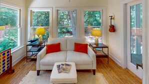 A living room with a white sofa, two red pillows, a coffee table with books, a lamp on a side table, and a guitar on the wall. - Hartnett Blvd 3502: 3  BR, 2  BA House in Isle of Palms, Sleeps 8 (Isle of Palms)