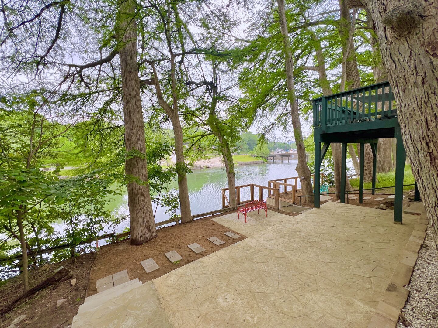 A stone deck with a red bench overlooking a lake, surrounded by trees.