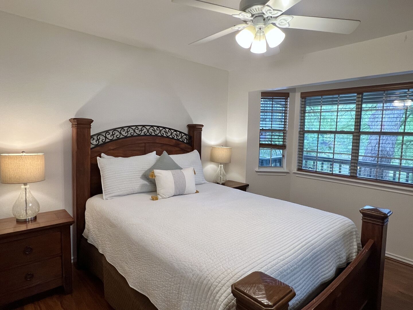 A neatly made bed with a wooden headboard, two bedside lamps, and a window with blinds.