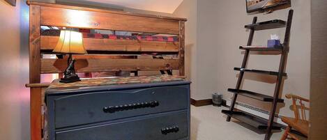 A bedroom with a wooden headboard, a dresser, a TV mounted on the wall, and a ladder shelf.