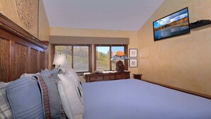 Une chambre à coucher avec un grand lit, une commode, une lampe et un téléviseur fixé au mur.