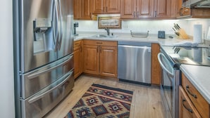 A modern kitchen with stainless steel appliances, wooden cabinets, and a built-in dishwasher. - Vail Village Condo, Walk to Golden Peak Lift/Ski School, Shops & Restaurants! (Vail)