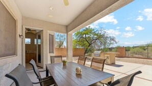 Eine überdachte Terrasse mit Tisch und Stühlen, einem Deckenventilator und Blick ins Grüne.