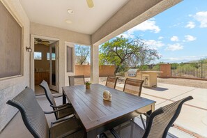 Un patio cubierto con mesa y sillas, un ventilador de techo y vistas al exterior.