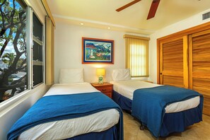 A hotel room with two beds, a window with a view of the street, a painting on the wall, and a wooden door.