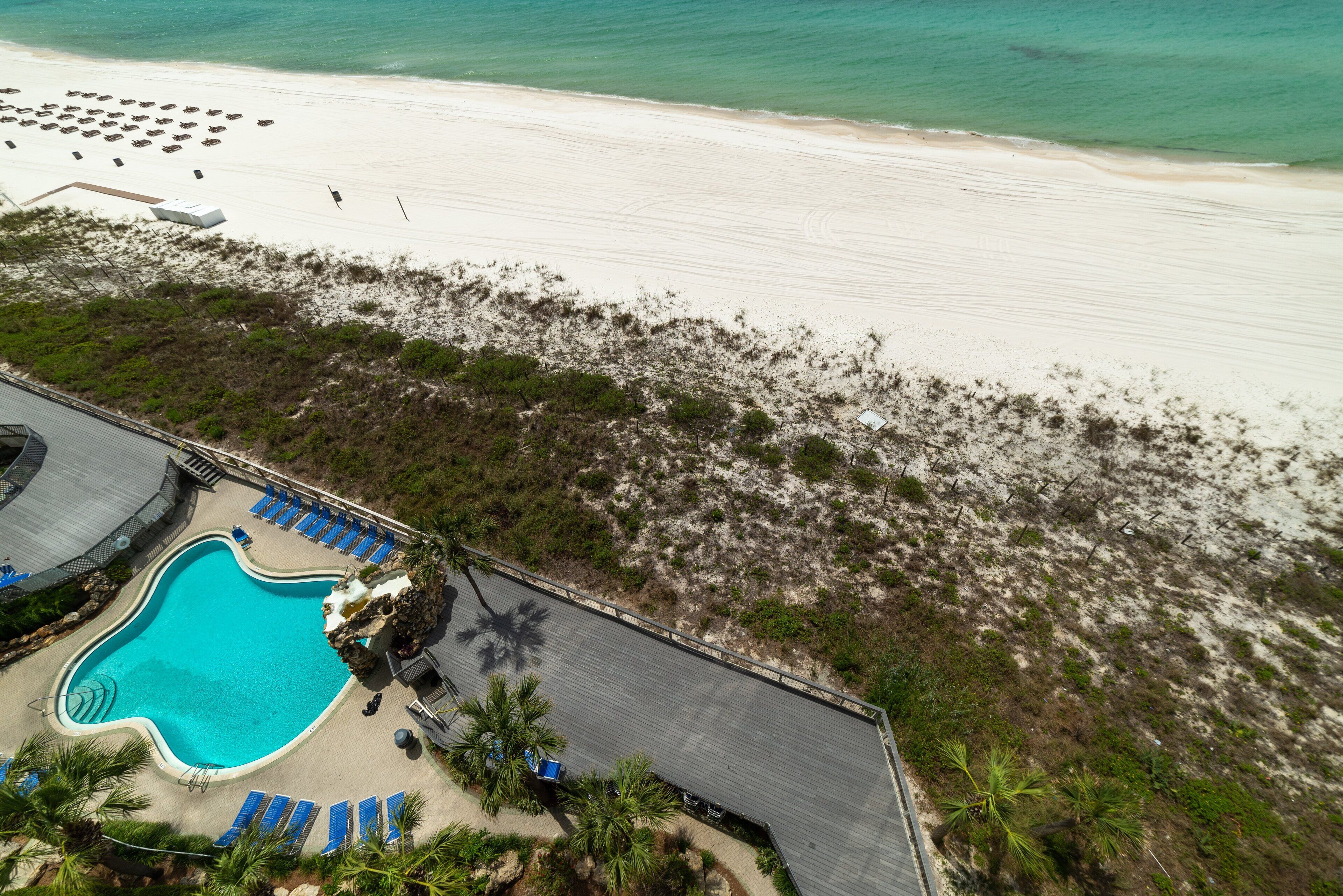 An aerial view of a resort with a swimming pool, beach, and lounge area.