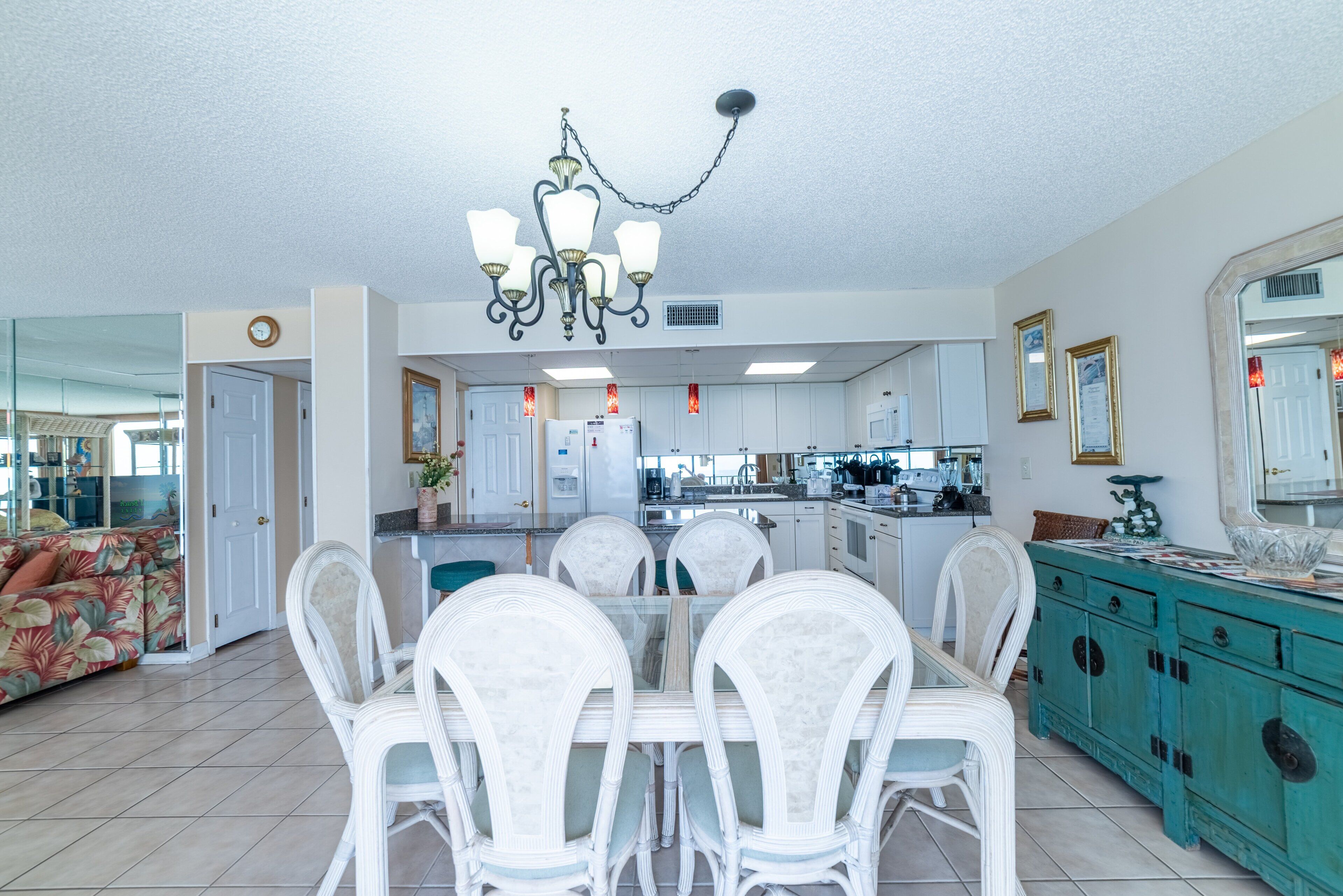 A spacious kitchen with white cabinets, a dining area with a glass table and white chairs, and a teal-colored cabinet with decorative items.
