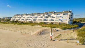 Een strandhotel met meerdere balkons, een zandstrand ervoor en een helderblauwe lucht.