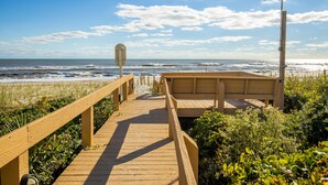 Een houten looppad dat naar een strand leidt, met een houten bankje en een bord.