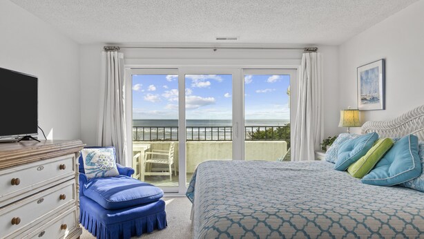 Een slaapkamer met een groot bed, een televisie, een dressoir en een balkon met uitzicht.