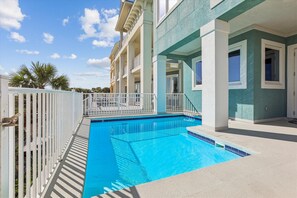 Relax by the pool surrounded by a white fence, overlooking the hotel's light blue exterior.